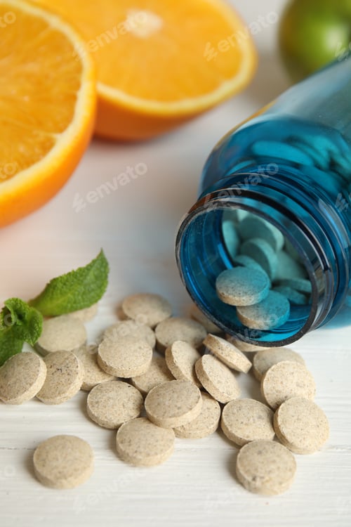 Preview: Bottle with vitamin pills and orange on white wooden table, closeup