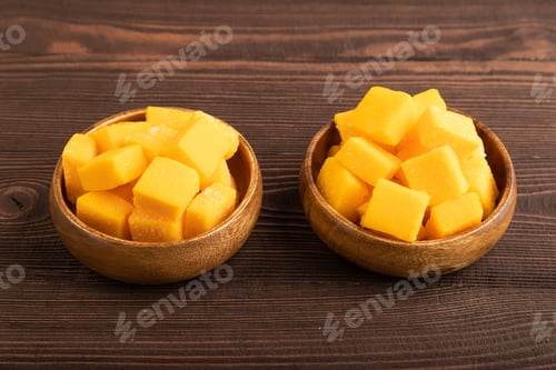 Preview: Dried mango cubes in wooden bowls on brown wooden, side view.