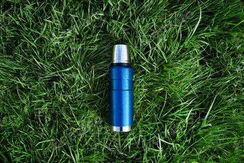 Preview: Blue vacuum thermos on green grass, top view. The concept of hiking, outdoor recreation, tourism