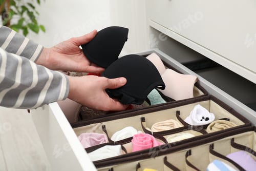 Preview: Woman putting bra into organizer in drawer at home, closeup