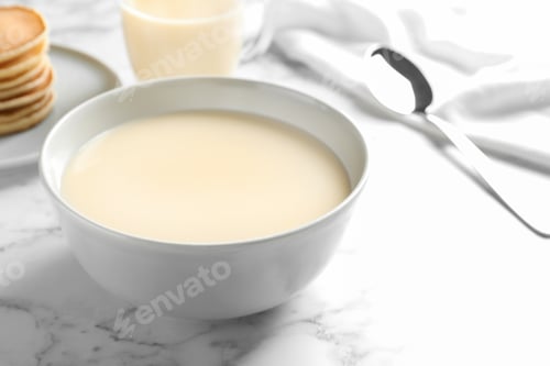 Preview: Bowl with condensed milk on marble table, space for text. Dairy products