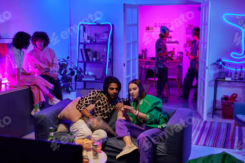 Preview: Young intercultural couple looking through new photos in mobile phone