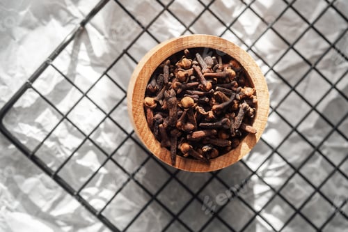 Preview: Cloves in a wooden bowl on a grid background showcasing their rich texture