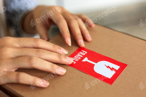 Preview: Woman Hand Sticking Fragile Mark Sticker to Parcel.