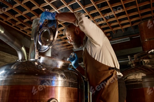Preview: Handsome adult brewer inspecting process of brewing beer with steam