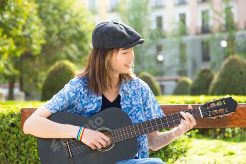 Preview: Young musician happily playing guitar in a park