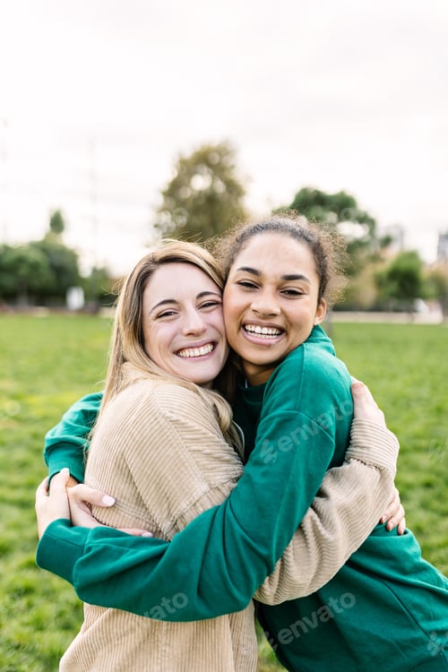 Preview: Vertical portrait of happy young women hugging each other outdoors