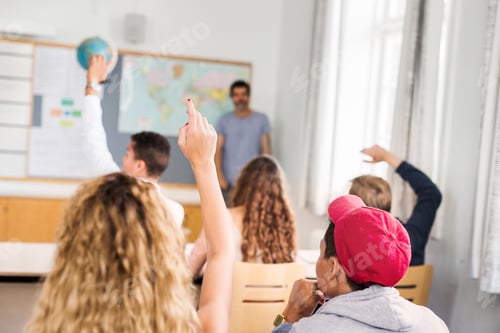 Vista previa: Students eagerly raising hands in a classroom with a teacher standing by the map