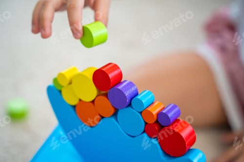 Preview: Little girl playing with wooden balancing toy on the floor in home living room. Focus on balancer