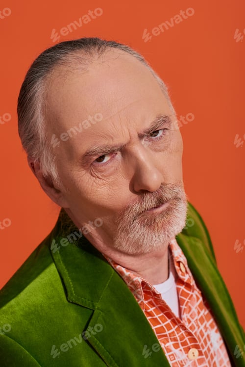 Preview: portrait of offended senior man with displeased face expression looking at camera on vibrant orange