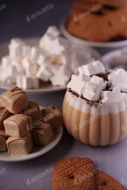 Preview: Indulgence: hot chocolate with marshmallows, fudge, biscuits, and foam on plates, indoors, cozy.