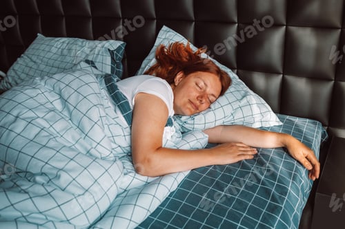 Preview: Beautiful young woman sleeping in the morning covered with blanket in bed at home bedroom