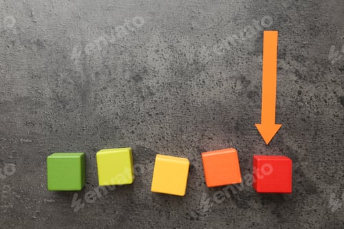 Preview: Maximum. Colorful cubes and arrow pointing at red one on grey table, flat lay