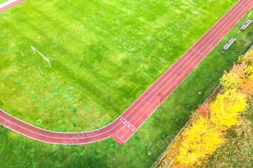 Preview: Aerial view of sports stadium with red running tracks and green grass football field