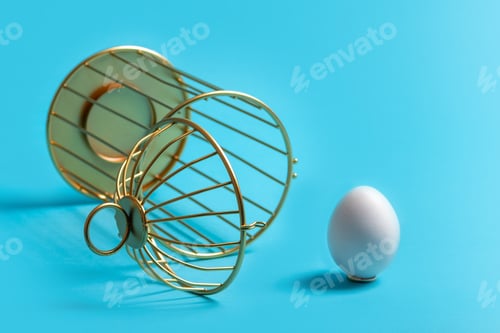 Preview: Upside down open cage with egg outside on a blue background. The concept of liberation from slavery.