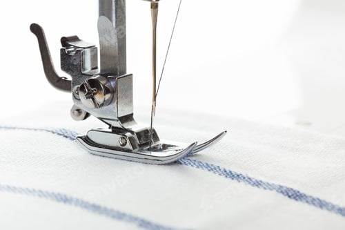 Preview: Sewing machine needle working on fabric with blue stripes in a well-lit workspace