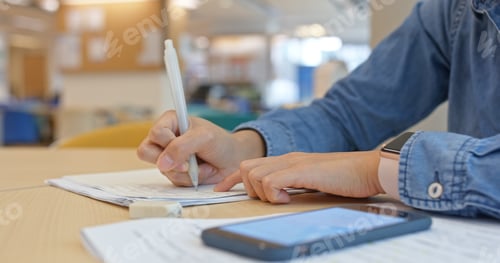 Preview: Woman do her paper with search on cellphone at school library