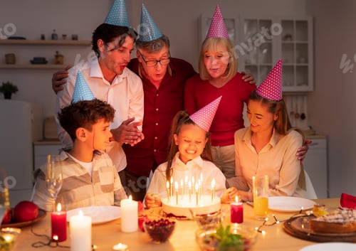 Preview: Joyful little girl receiving tasty birthday cake with candles from loving family, celebrating b-day