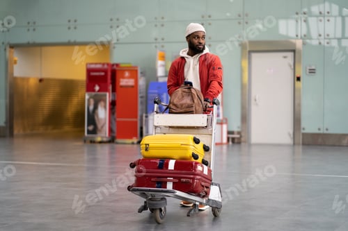 Preview: Black man pushing luggage trolley walking after arrival at airport terminal. Vacation, journey.