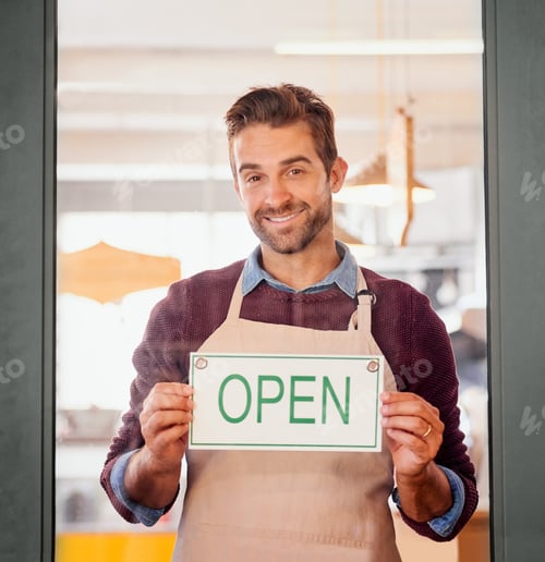 Preview: Portrait of a young business owner standing in the doorway of his coffee shop with an open sign