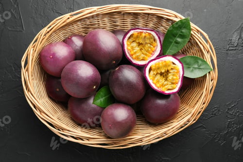 Preview: Fresh passion fruits with green leaves in wicker basket on grey textured table, top view