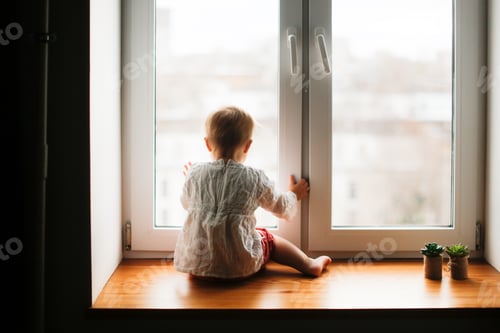 Preview: Cute caucasian infant toddler child sitting on the window with his back