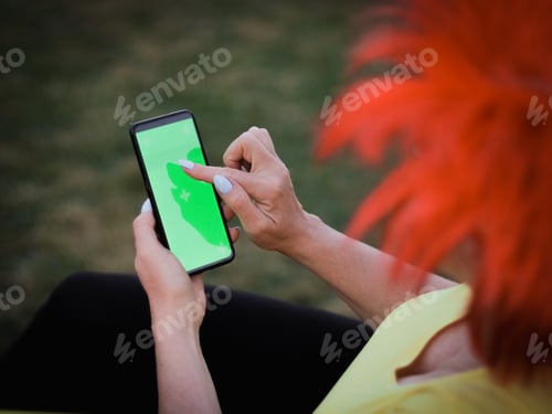 Vista previa: Mujer caucásica con una peluca de bandera belga sosteniendo un smartphone con una pantalla verde apuntando su aleta