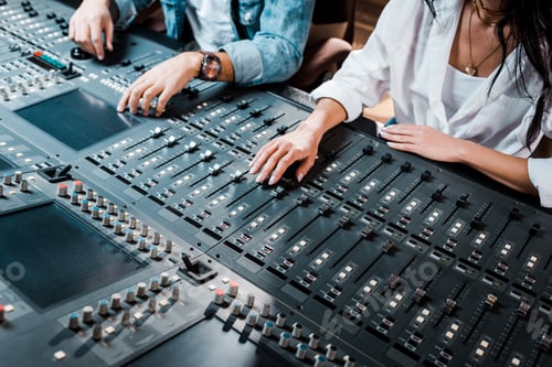 Preview: cropped view of two multicultural sound producers working at mixing console in recording studio