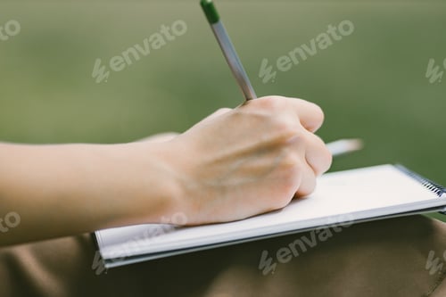 Preview: Cropped photo of a woman's hand with a pensil writing in a notebook