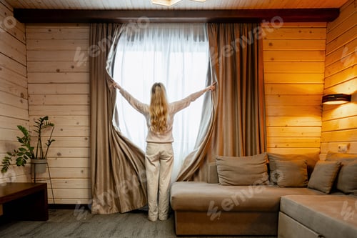 Preview: Woman opening curtains in cozy wooden house, embracing new day and morning light