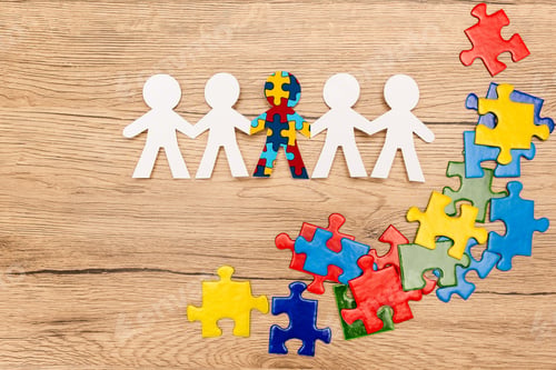 Preview: Top view of special kid with autism among another and pieces of bright colorful puzzle on wooden