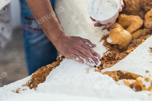 Preview: Female hand spreading white paste on the rough surface of a polystyrene figure.