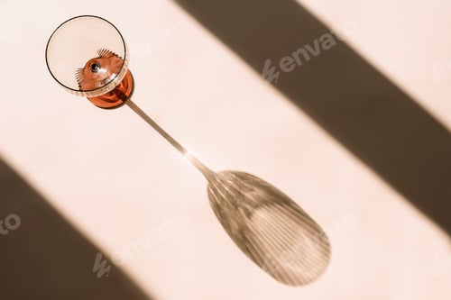 Preview: Elegant glass casting a long shadow on a light surface, minimal abstract composition