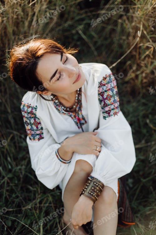 Preview: Young woman in traditional national embroidered shirt and skirt on nature at sunset.