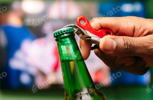 Preview: African American man watching football game and opening a beer in a green bottle