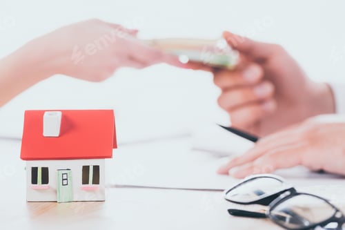 Preview: partial view of businessman taking money from client near house model on tabletop
