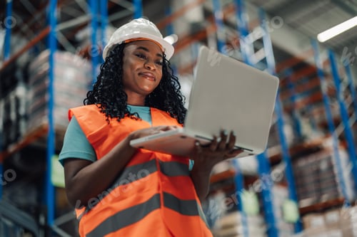 Preview: Happy african american female warehouse worker with laptop, looking satisfied.