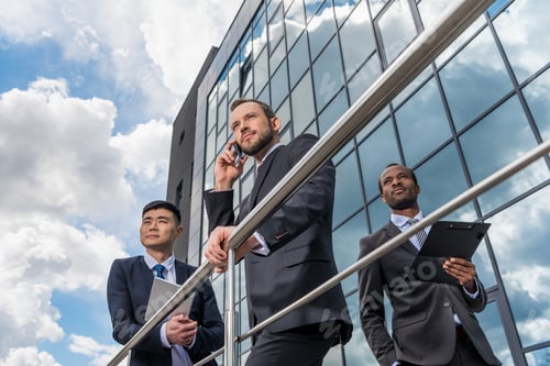 Preview: multicultural business team meeting and using smartphone and digital tablet outdoors near office