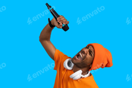 Preview: Portrait of a young man singing with microphone and headphones on blue background