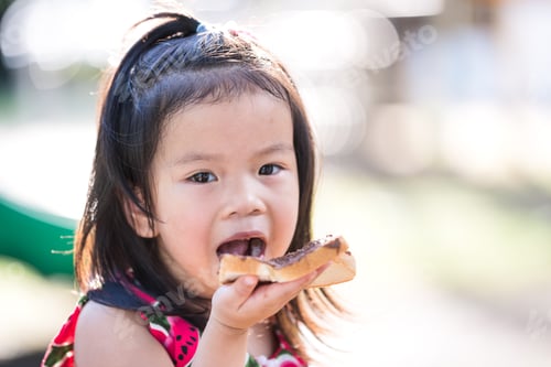 Preview: Cute kid girl enjoys eating bread with sweet chocolate. Child aged 4 years old. Empty space for text