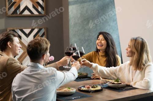 Preview: Two intercultural couples in smart casualwear clinking with glasses of red wine