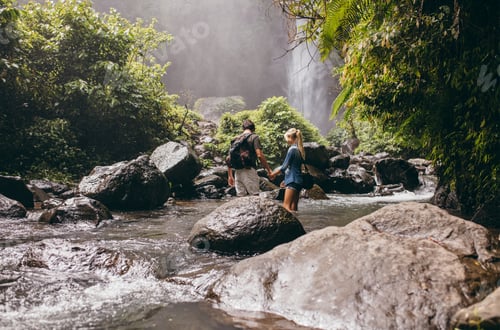 Preview: Young couple crossing stream in forest