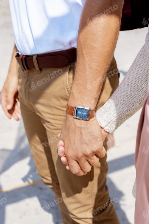 Preview: partial view of couple holding hands while walking on sandy beach
