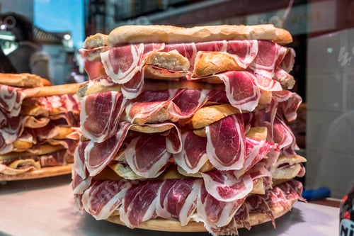 Preview: Several jamon serrano sandwiches piled up in a shop window, conceptual image