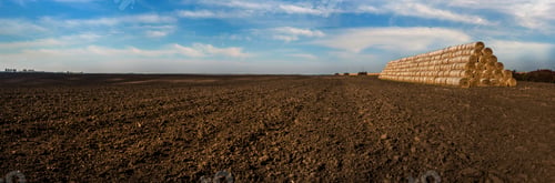 Preview: panoramic view of straw bales stacked in a pyramid shaped pile on a plowed field, arable land