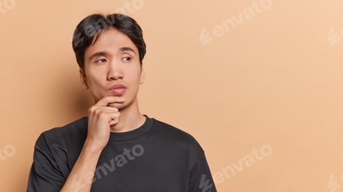 Preview: People emotions concept. Young thoughtful Asian man holding left hand on chin trying to solve