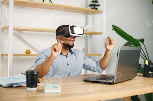 Preview: Black male entrepreneur sitting in office and using virtual reality glasses