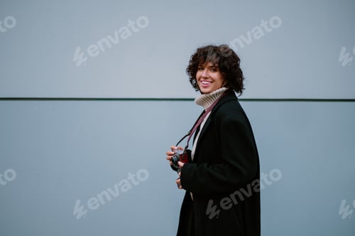 Preview: Young woman holding her old retro camera while having a big smile on her face.
