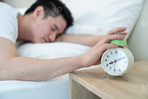 Preview: Asian attractive young man turn off alarm clock ringing in the morning.