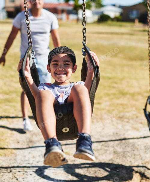 Preview: Portrait of a cheerful little boy swinging on a swing outside in a park during the day